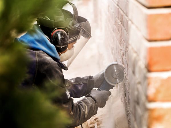 Arbeiter schleift Mauerwerk mit Schutzkleidung und Winkelschleifer ab