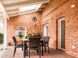 Moderne überdachte Terrasse mit rustikaler Klinkerwand und Esstisch